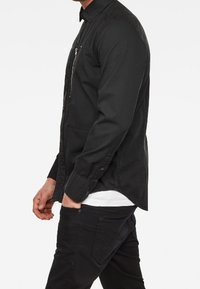 Svart knäppskjorta med en dragkedjeficka, långa ärmar och en slim fit. Tillverkad av ett glatt tyg med en slät struktur.