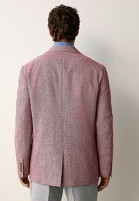 Blazer en lin rouge avec une finition texturée, fente unique au dos et poignets boutonnés. Dispose d'un revers cranté et d'une coupe slim.