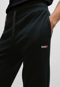 Svarta sweatpants med dragsko i midjan och sidfickor. Broderad "HUG❤️" logotyp i vitt och rött på vänster lår.