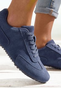 Navy blue suede sneakers with lace-up design, rounded toe, textured surface, and rubber sole featuring small studs for grip.
