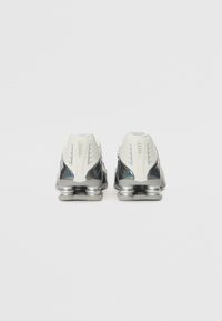 Zwart-witte sportiviteitsschoenen met zilveren accenten. Beschikt over een gestructureerde bovenkant en een kenmerkend hielontwerp voor demping.