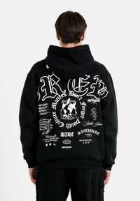 Czarny hoodie z różnymi białymi nadrukami graficznymi i tekstem. Materiał wydaje się miękki, z luźnym krojem i kapturem ze sznurkiem.