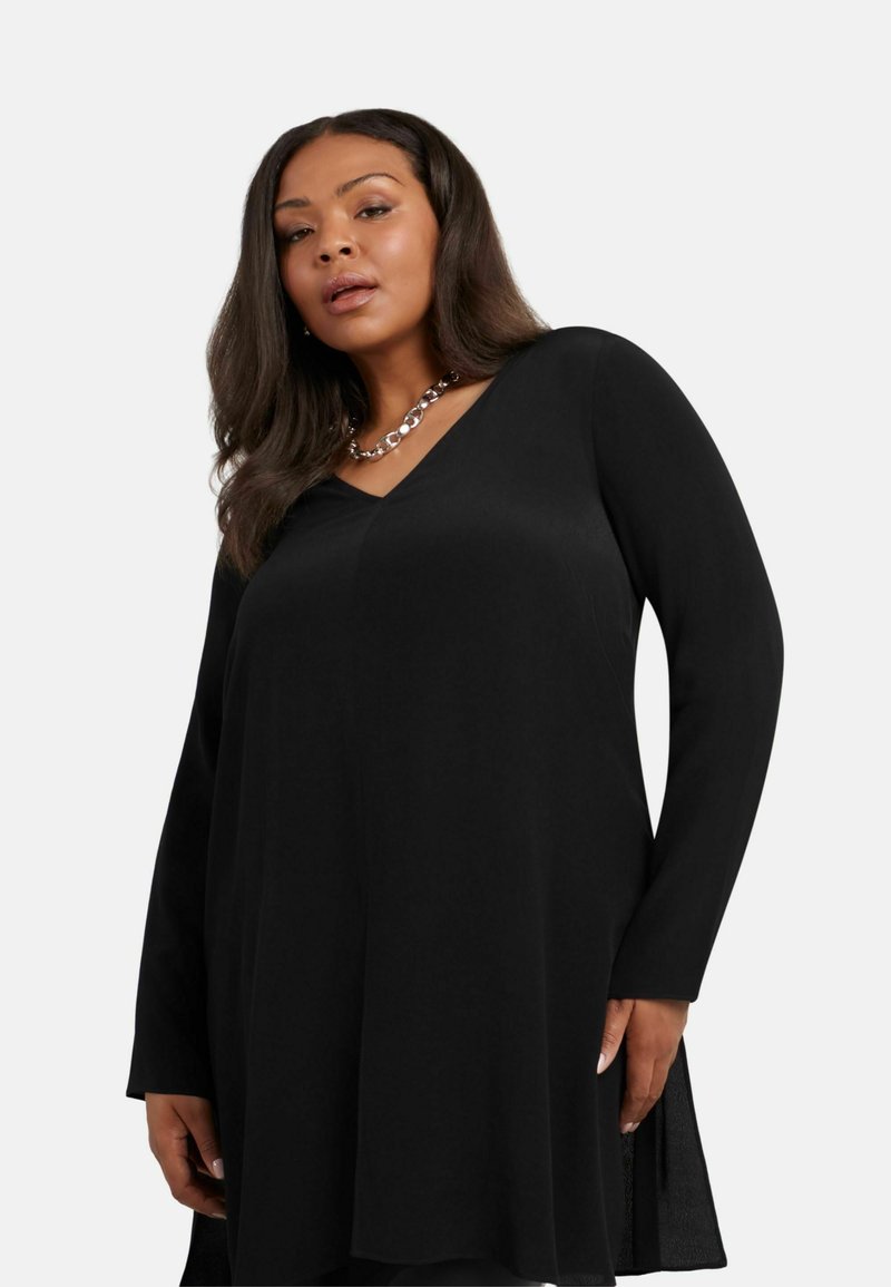 Svart långärmad tunika med V-ringning, tillverkad av ett mjukt tyg, med sidokilar och en avslappnad passform. Accenterad med kedjesmycken.