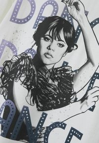 Hvid grafisk t-shirt med en sort og grå illustreret figur, med volantsærmer, prydet med lilla og blå tekst der staver "DANCE."