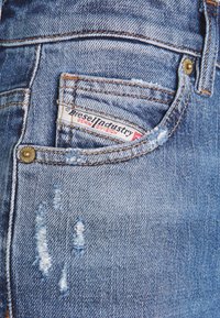 Jean en denim bleu délavé avec des détails usés, une petite poche et une étiquette de marque indiquant "Diesel Industry Denim Division".