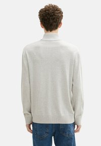 Heller grauer Pullover, weiches Strickmaterial, hoher Kragen, gerippter Saum und Bündchen, lockere Passform, kombiniert mit blauen Jeans, minimalistischem Design.