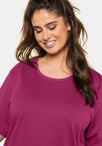 T-shirt a maniche corte e colletto rotondo di un vivace magenta, realizzato in un tessuto morbido con una texture liscia, con vestibilità comoda e un leggero rigatino.