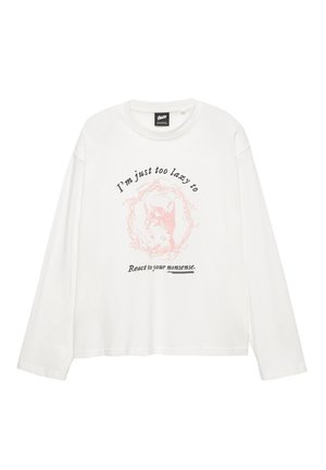 Fehér, hosszú ujjú póló puha anyagból, világos rózsaszín grafikával díszített macskaképpel, fekete szöveggel a kép felett és alatt.