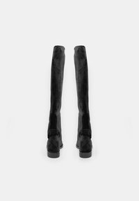 Botas negras por encima de la rodilla con una textura de ante suave, diseño ajustado y punteras redondeadas. Presentan un tacón bajo y detalles de costura lateral.