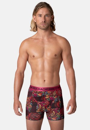 Patroonboxers met een roze tailleband met de tekst "MUCHACHO MALO." Het ontwerp bevat kleurrijke bloemen- en dierenmotieven op een donkere achtergrond.