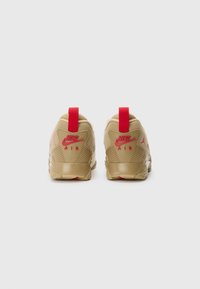 Bežās Nike Air sneakeres ar sarkaniem akcentiem, ar teksturētu apdari, mīkstu apkaklīti un papēža cilpu. Zolei redzams protektora raksts.