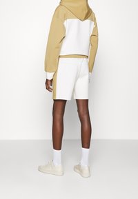 Ljusbeige och vit hoodie med en kontrasterande övre panel, tillsammans med vita shorts. Materialet verkar vara mjukt och elastiskt.