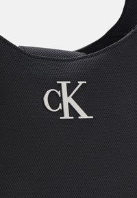 Borsa nera realizzata in materiale testurizzato con un logo silver "cK" in evidenza sulla parte anteriore. Design semplice e moderno con una forma curva.
