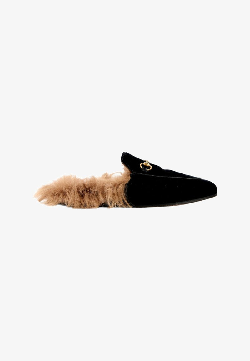 Mocassin noir en velours sans talon avec détail de boucle dorée et doublure en fourrure beige qui s’étend de l’intérieur jusqu’au talon.