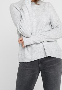Lichtgrijze gebreide trui met een ronde hals en lange mouwen, met een ontspannen pasvorm en geribde manchetten, gecombineerd met donkergrijze jeans.