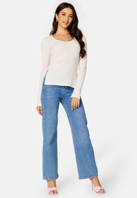 Helles, geripptes Langarmoberteil mit Rundhalsausschnitt, kombiniert mit blauen Weitbeinjeans und rosa offenen High Heels.