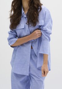 Camicia a righe blu e bianche con bottoni e due taschini sul petto, abbinata a pantaloni larghi coordinati, caratterizzati da una trama morbida.