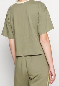 Olivově zelené tričko s krátkým rukávem a cropped střihem, vyrobené z jemné bavlny. Má kulatý výstřih a volný střih, spárované s odpovídajícími kalhotami.