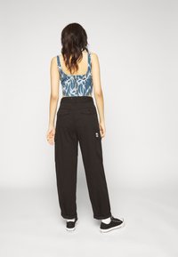 Mustat cargo-housut, joissa on sivutaskut ja rento leikkaus. Yläosa on sinikuvioinen crop-top, jossa on pyöreä selkäosa. Mustat tennarit täydentävät asua.