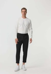 Cămașă albă cu mânecă lungă și decolteu rotunjit, asortată cu pantaloni negri cu manșete răsucite și adidași albi. Design simplu, ajustat.