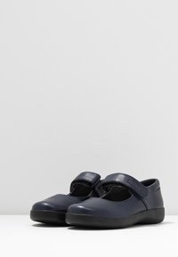 Zapatos Mary Jane de cuero azul marino con una amplia correa de velcro, punta redondeada y suela de goma negra. Textura suave con un detalle mínimo.