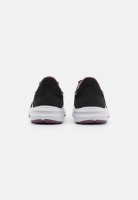Chaussures de sport noires avec des accents violets, tige en mesh, semelle blanche rembourrée et design de talon distinct. Vue arrière montrant le système de laçage et la structure.