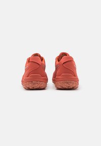 Zapatillas deportivas rojas con una superficie texturizada, talón acolchado y suela de goma con patrones de tracción; acentos reflectantes en los lados.