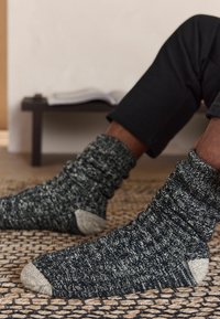 Gestrickte Socken mit einem dunkelgrauen, weiß gesprenkelten Muster und hellgrauen Zehenakzenten. Sie verfügen über ein geripptes, strukturiertes Design für zusätzliche Wärme.