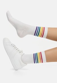Witte crew-sokken met veelkleurige strepen in rood, oranje, geel, groen, blauw en paars, gecombineerd met witte sneakers.