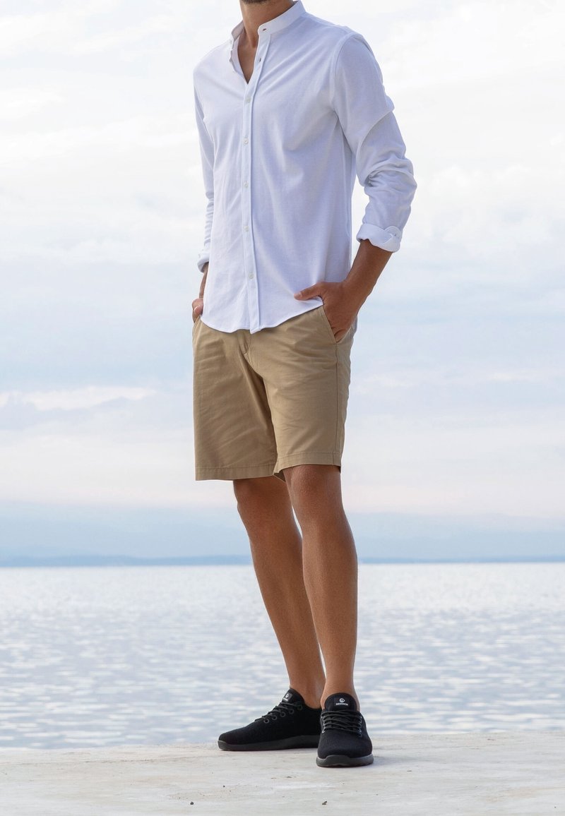 Biała, długorękawowa koszula na guziki, khaki krótkie spodenki i czarne trampki. Koszula ma luźny kołnierz; spodenki sięgają kolan; trampki mają teksturowaną powierzchnię.