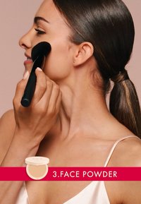 Compatto di cipria con coperchio color crema mostrato accanto a una donna che applica la cipria sulla guancia usando un pennello da trucco nero.