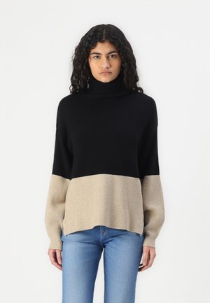 Maglione a collo alto in nero e beige con texture a costine. Vestibilità comoda con spalle scese e spacchi laterali. Abbinato a jeans chiari.
