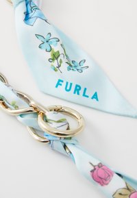Vaaleansininen silkkihuivi, jossa on kukkakuosi ja kultaiset yksityiskohdat. Huivissa on sana "FURLA" rohkealla turkoosilla kirjasimella.