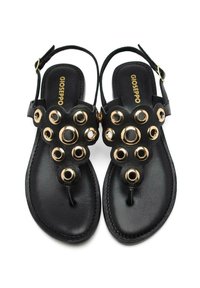 Sandalias negras con un diseño floral y acentos circulares en tono dorado, suela plana y correa ajustable en el tobillo para un ajuste seguro.