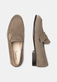 Wildleder-Lederslipper in Taupe mit einer Mokassin-Zehenpartie und einem dekorativen Riemen über dem Spann. Flache schwarze Außensohle für Stabilität. Hergestellt in Italien.