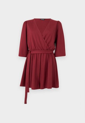 Φόρεμα τύπου wrap σε βουργουνδί χρώμα, με V-λαιμόκοψη, φουσκωτά μανίκια τριών τετάρτων και ζώνη από το ίδιο ύφασμα δεμένη στη μέση.