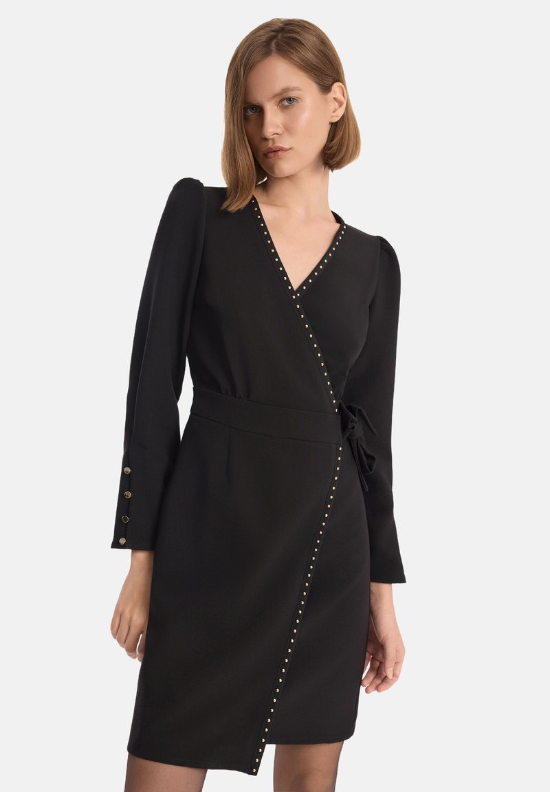 Czarna sukienka o kroju kopertowym z długimi rękawami, dekoltem w serek i złotymi nitami wzdłuż przodu. Tkanina ma gładką teksturę.