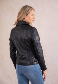 Black leather jacket with a fitted design, quilted shoulder detail, and a belted waist. Paired with light blue denim jeans.