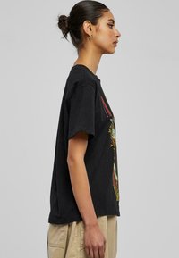 Sort bomulds T-shirt med korte ærmer, der har et farverigt grafisk design på forsiden. Boxy fit, rund halsudskæring, glat tekstur.