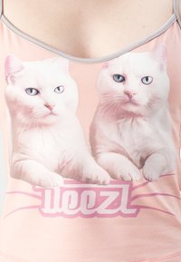 To hvite katter med blå øyne som hviler potene på rosa teksten "Deezl" på en ferskenfarget tank topp.