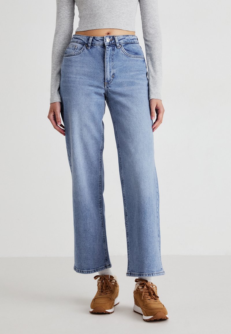 Light blue wide-leg jeans with a high waist, featuring two front pockets and a zip fly. Worn with brown sneakers and a gray long-sleeve top.
