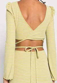 Vihreä vaaleanvihreä kääntöpäällys, jossa valkoisia raitoja, pitkät hihat, joissa on röyhelöhuiput, V-mallinen selkäosa, vyötärölle sidottu yhteensopivalla nauhalla.