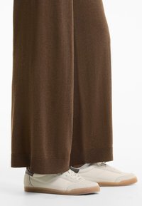 Sneakers bianchi con una tomaia strutturata grigio chiaro e una punta in suede beige, abbinati a pantaloni in maglia marroni larghi con polsini a coste sulle caviglie.