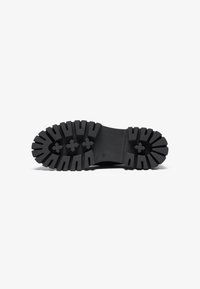 Black rubber shoe sole with deep treads, featuring an embossed logo and star-like patterns for improved traction and stability.