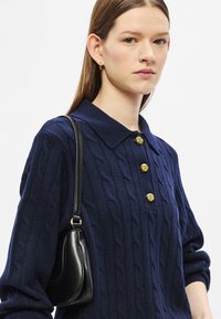 Μπλε πουλόβερ πλεκτό με καλώδιο με κλασικό γιακά, διακοσμητικά χρυσά κουμπιά και μαύρη τσάντα ώμου με καμπυλωτό σχήμα και διακριτική λάμψη.