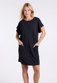 Črna obleka do kolen iz mehkega materiala, z okroglim izrezom, kratkimi rokavi in dvema sprednjima žepoma. Gladka tekstura, sproščen kroj.