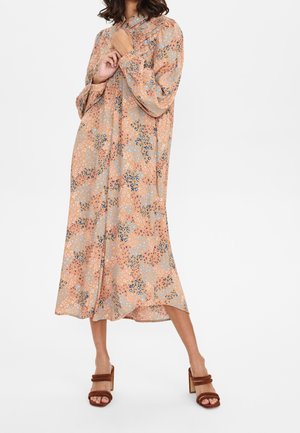 Femme portant une robe midi ample à manches longues boutonnée avec un imprimé floral pêche, bleu et noir et des sandales à talons marron.
