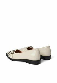 Ballerines en cuir verni beige avec un bout ouvert, dotées d'une boucle argentée ajustable et d'accents en clous à l'avant. Semelle en caoutchouc noire.
