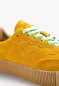 Sneaker giallo in suede con lacci verde chiaro, suola in gomma testurizzata e logo teschio impresso sul lato. Fodera interna liscia.