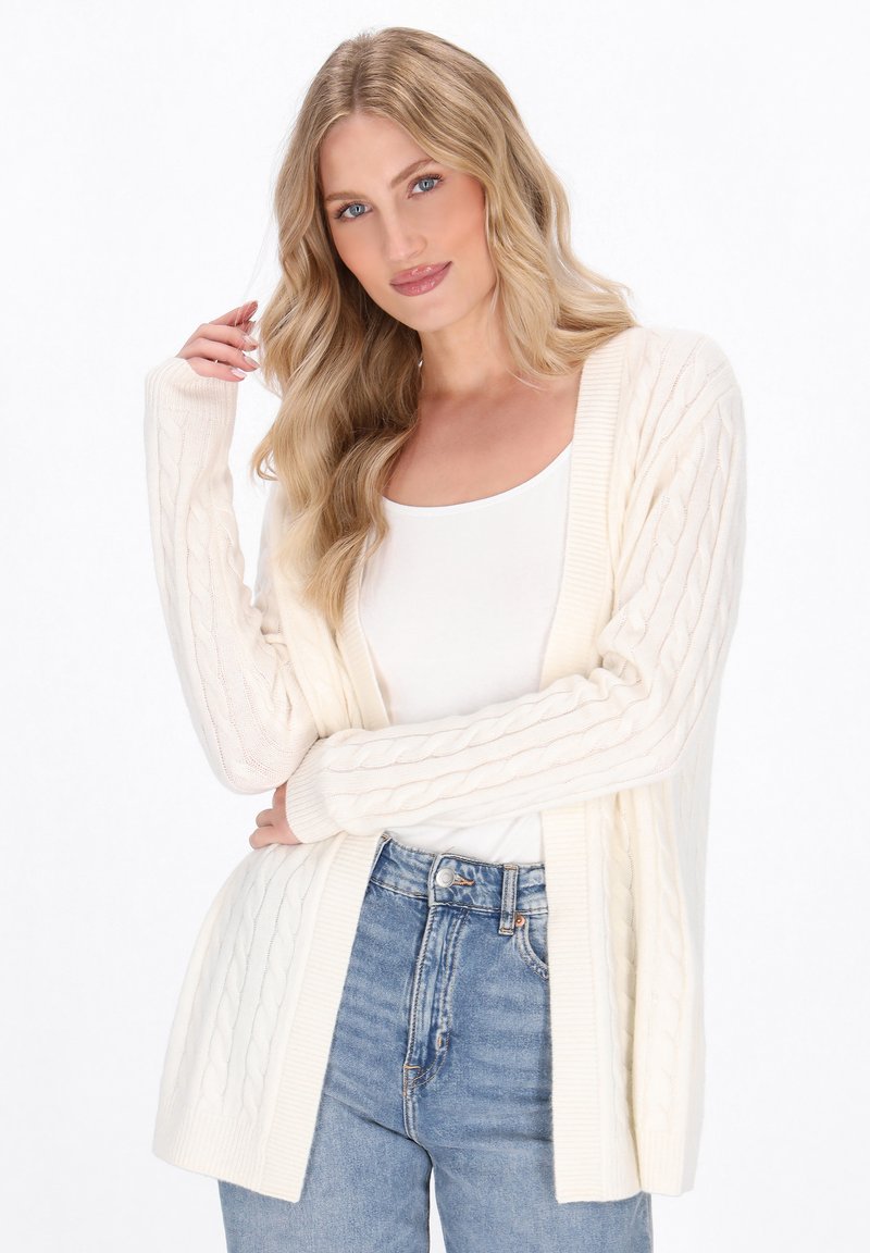 Cremefarvet kabelstrikket cardigan med åben front, lange ærmer og ribbede kanter, parret med en hvid top og denim jeans.